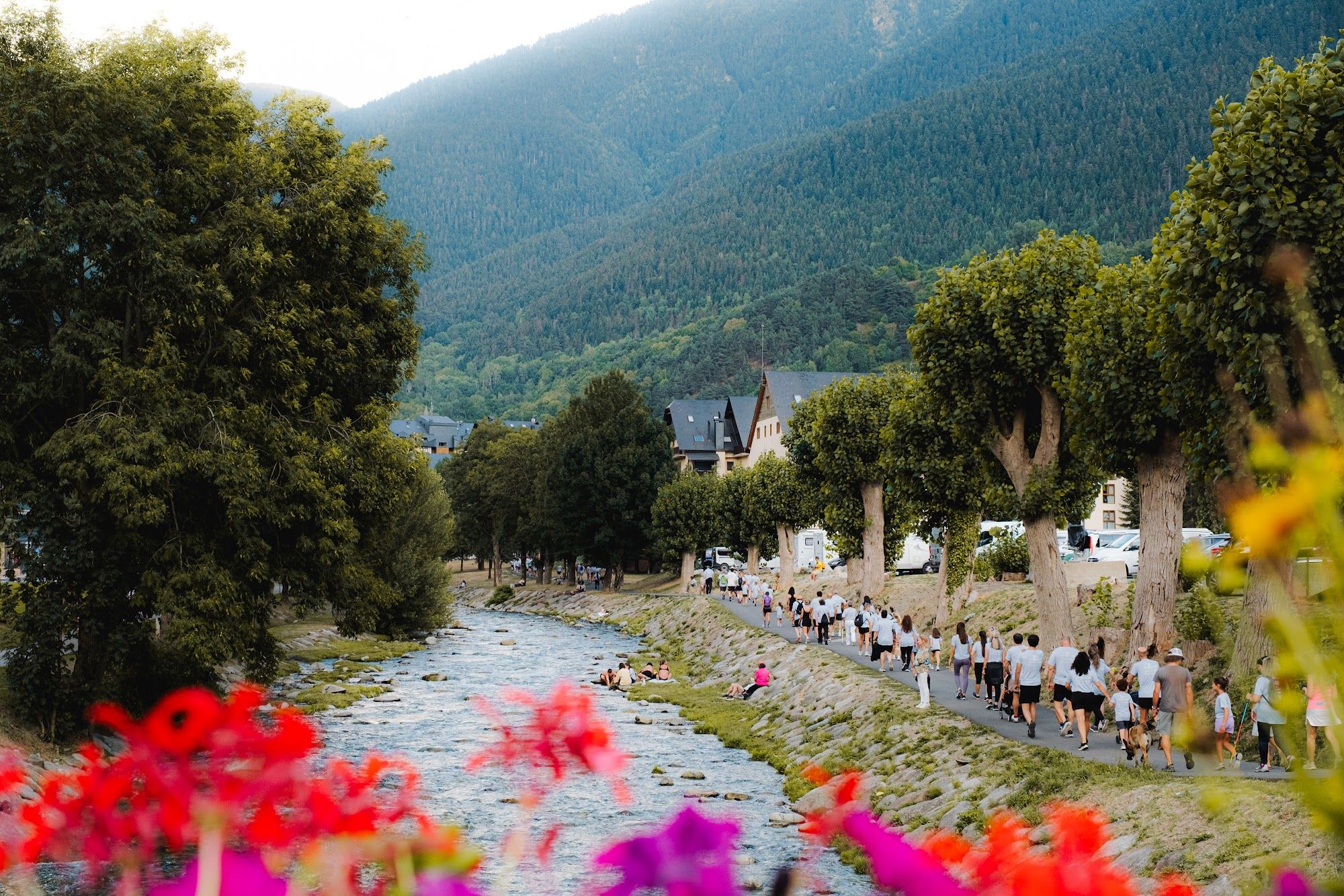 El río a su paso por Vielha, con flores en primer plano y caminantes al fondo